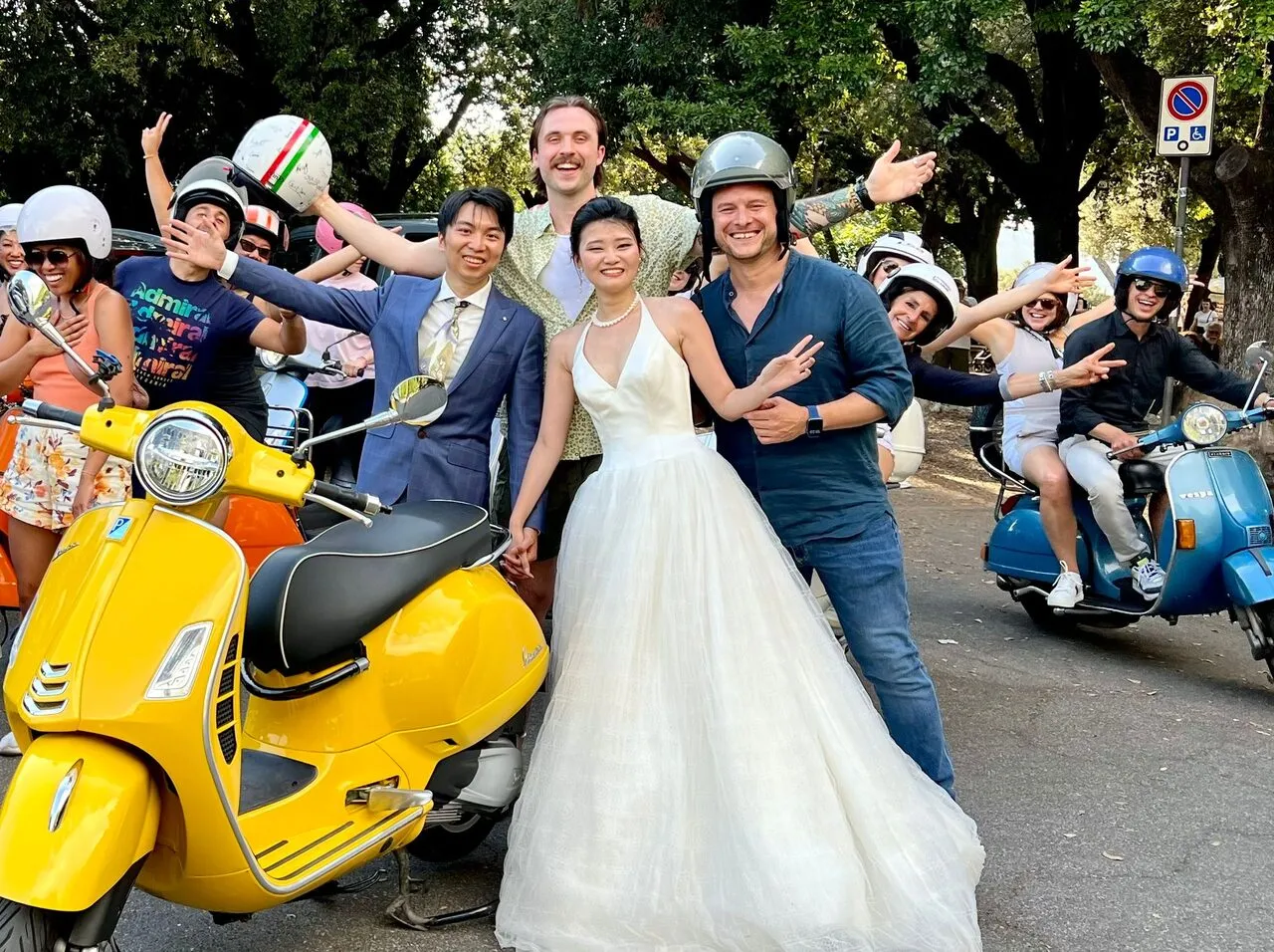 Sposi in posa con una Vespa gialla insieme al gruppo del tour