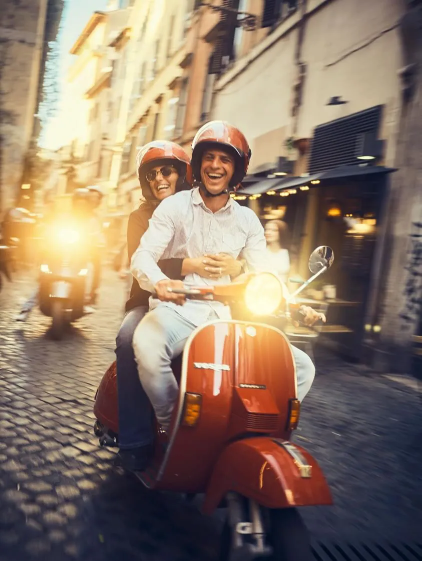 Coppia in Vespa tra i vicoli illuminati del centro storico al tramonto