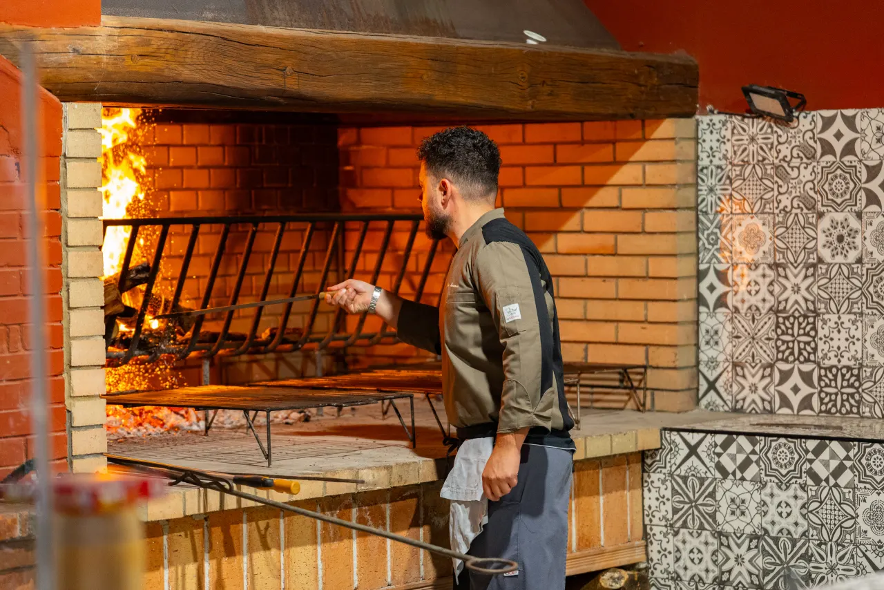 Lo chef accudisce il fuoco del grande camino a legna